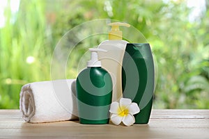Different shower gel bottles with towel and plumeria flower on wooden table