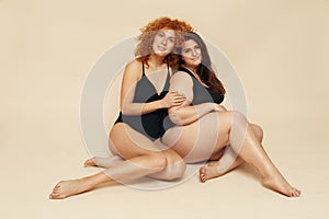 Different Size. Diversity Women Portrait. Female Friends Sitting On Floor. Smiling Brunette And Redhead In Black Bodysuits. photo