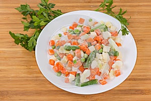 Different sliced frozen vegetables on dish on wooden surface photo