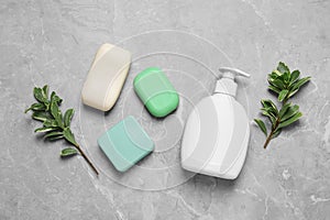 Different soap bars, dispenser and green plants on light grey table, flat lay