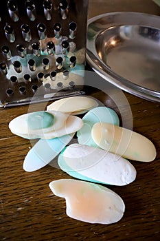 Different soaps and remnants on wooden table with metal grater and dish, preparation for grated soap, lot of solid soap for hygien