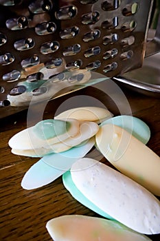 Different soaps and remnants on wooden table with metal grater and dish, preparation for grated soap, lot of solid soap for hygien