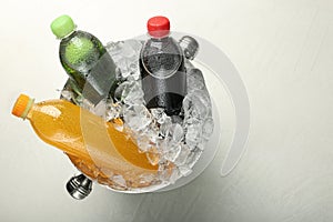 Different soda drinks in metal bucket with ice on grey table, top view