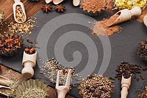 Different spices in bakeware with wooden scoops on the slate slone background