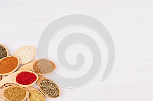 Different spices in bamboo spoons on white wood background, top view, closeup.