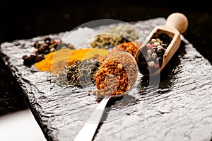 Different spices and herbs on a black slate. Iron spoon with chili pepper. Indian spices. Ingredients for cooking. Healthy eating