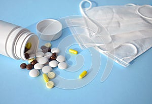 Different spilling pills, medication bottle and masks on blue background.