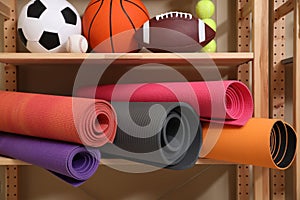 Different sport balls and yoga mats on rack indoors