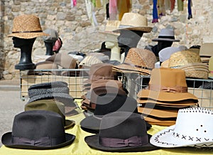 Different style men hats on a shelf of a street market. On background, manikin heads wearing straw hats