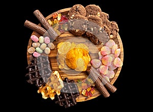 Different sweet and delicious candies on a wooden plate on a black background with chips, cockies, gummibears waffles, chocolate