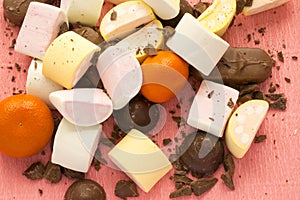 Different sweets and citrus on pink background: marshmellows, zephyr, chololate and tangerine.