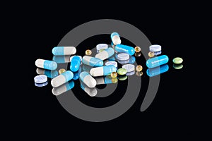 Different tablets, pills and capsules of different colors on an isolated black background with reflection