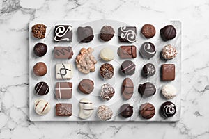 Different tasty chocolate candies on marble table, flat lay