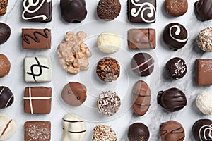 Different tasty chocolate candies on marble table, flat lay