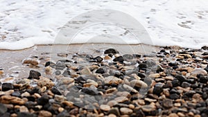 Different texture on the beach - water and sand, stones and pebbles, waves and splashes