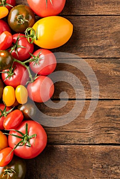 Different tomatoes on rustic wooden background with copyspace.