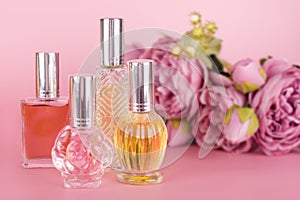 Different transparent perfume bottles with bouquet of peonies on pink background. Aromatic essence bottles with spring flowers.