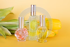 Different transparent perfume bottles with bouquet of tulips on yellow background. Aromatic essence bottles with spring flowers.