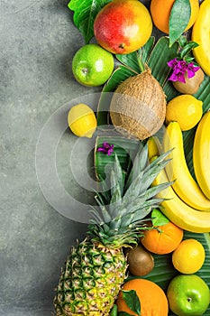 Different Tropical Summer Fruits. Pineapple Mango Coconut Citrus Oranges Lemons Apples Kiwi Bananas on Dark Stone Background