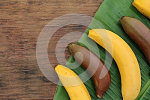 Different types of bananas and fresh leaf on wooden table, flat lay. Space for text