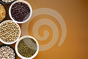 Different types of beans in bowls on orange background