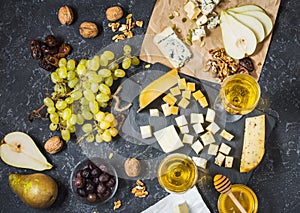 Different types of cheese on board, olive, fruits, almond and wine glasses on black stone table