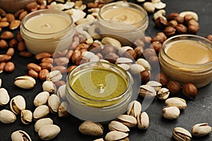 Different types of delicious nut butters and ingredients on black table