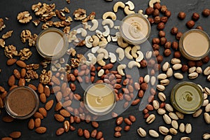 Different types of delicious nut butters and ingredients on black table, flat lay