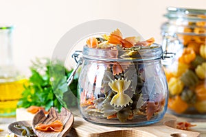 Different types of italian pasta in glass jars on a yellow wooden table. Colored natural paste. Spinach, Beetroot, Egg