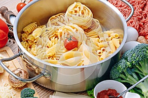 Different types of italian pasta on a wooden background with various ingredients for cooking traditional italian dishes