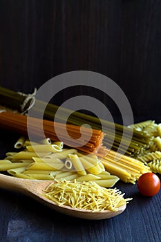 Different types of Italian pasta with a wooden spoon on a table with copy space