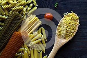 Different types of Italian pasta on a wooden table with wooden spoon