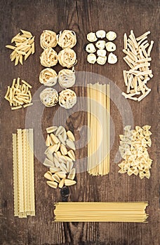 Different types of Italian uncooked pasta on rustic wooden table background, top view.