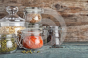 Different types of legumes and cereals in glass jars on wooden table, space for text. Organic grains