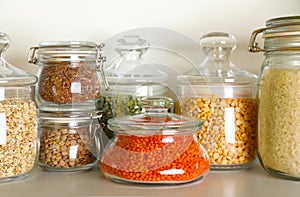 Different types of legumes and cereals in jars on table