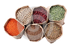 Different types of legumes and cereals in paper bags on white background, top view. Organic grains