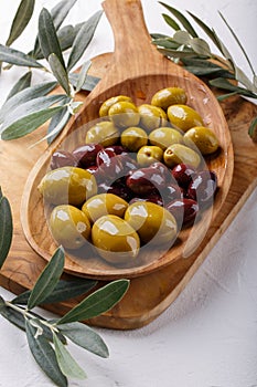 Different types of olives green and black on wooden plate on white table. Close-up