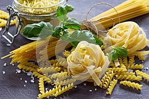 Different types of pasta with basil on the kitchen wooden table. The concept of Italian food