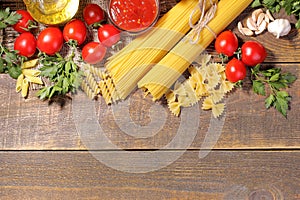 Different types of pasta with cherry tomatoes, olive oil, parsley on a brown wooden background.