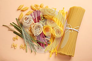 Different types of pasta on light orange background, flat lay