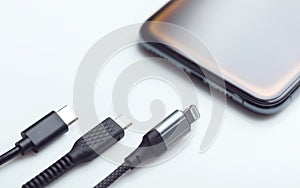 Different types of phone charging cables are lined up next to a smartphone. The image represents the concept of comparing charging photo