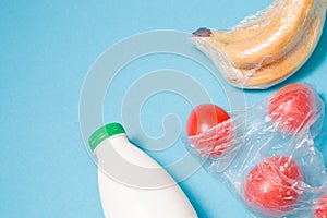 different types of plastic packaging on a blue background, a package with tomatoes, bananas wrapped in a film and a bottle of milk