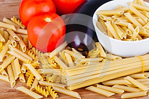 Different types of raw Italian pasta with tomatoes and other vegetables, top view background. Selected focus.