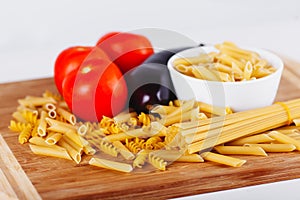 Different types of raw Italian pasta with tomatoes and other vegetables, top view background. Selected focus.