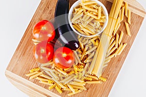 Different types of raw Italian pasta with tomatoes and other vegetables, top view background. Selected focus.