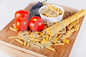 Different types of raw Italian pasta with tomatoes and other vegetables, top view background. Selected focus.