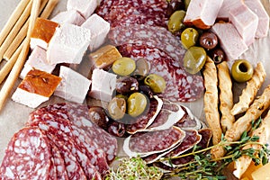 Different types of salami, olives, greens, breadsticks.