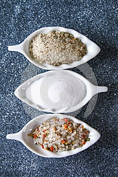 Different types of salt in glass bowls on a dark gray table.