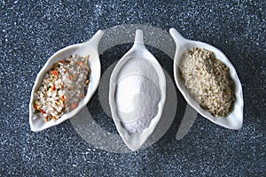 Different types of salt in glass bowls on a dark gray table.