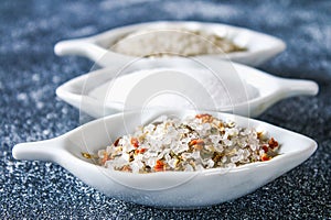 Different types of salt in glass bowls on a dark gray table.